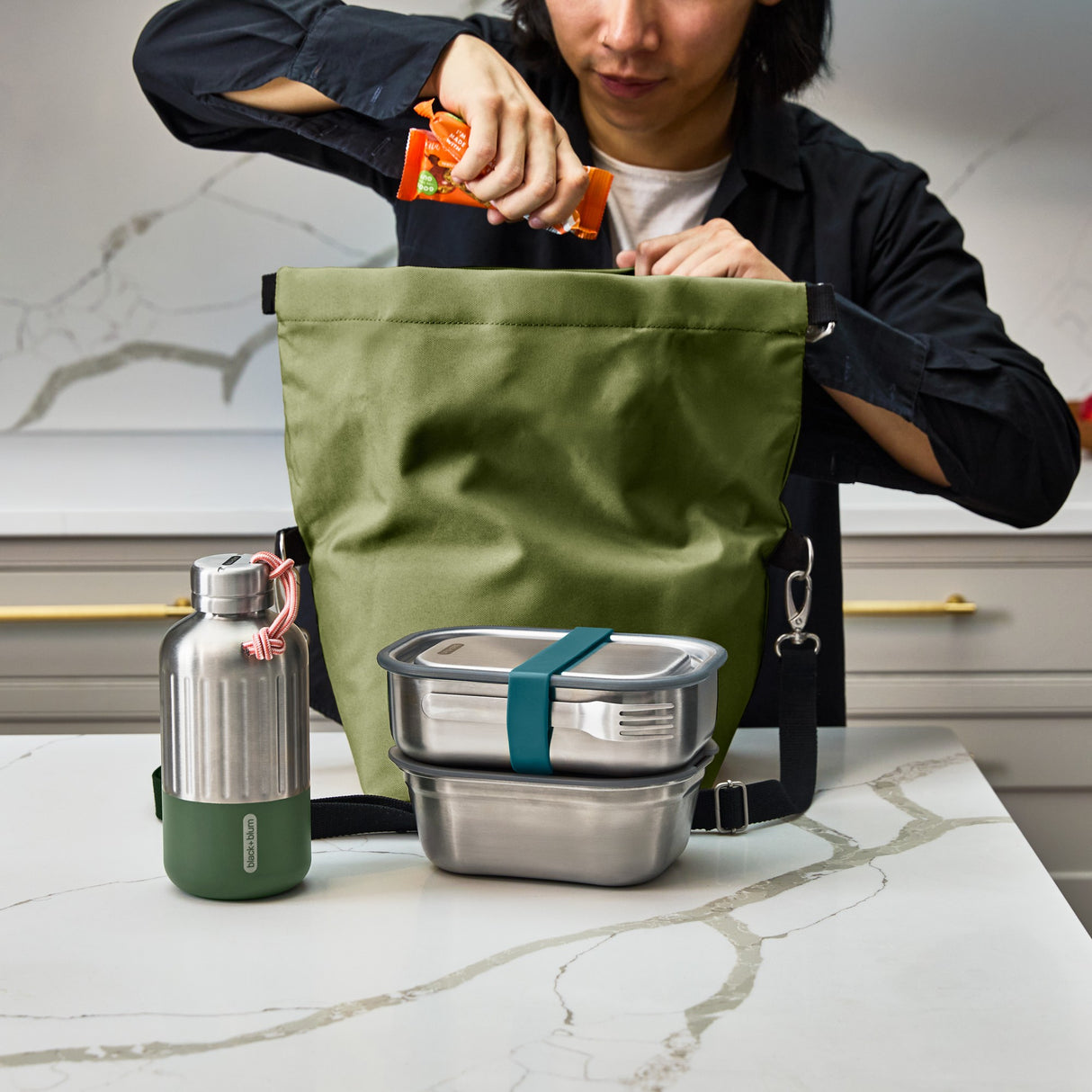 Black+Blum insulated lunchbag open on a counter, showing interior space and moss-green accents, designed for carrying meals comfortably.