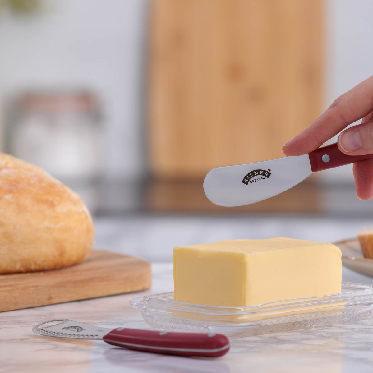 KILNER buttermesser with red handle and two grips, designed for spreading and handling butter or soft spreads.